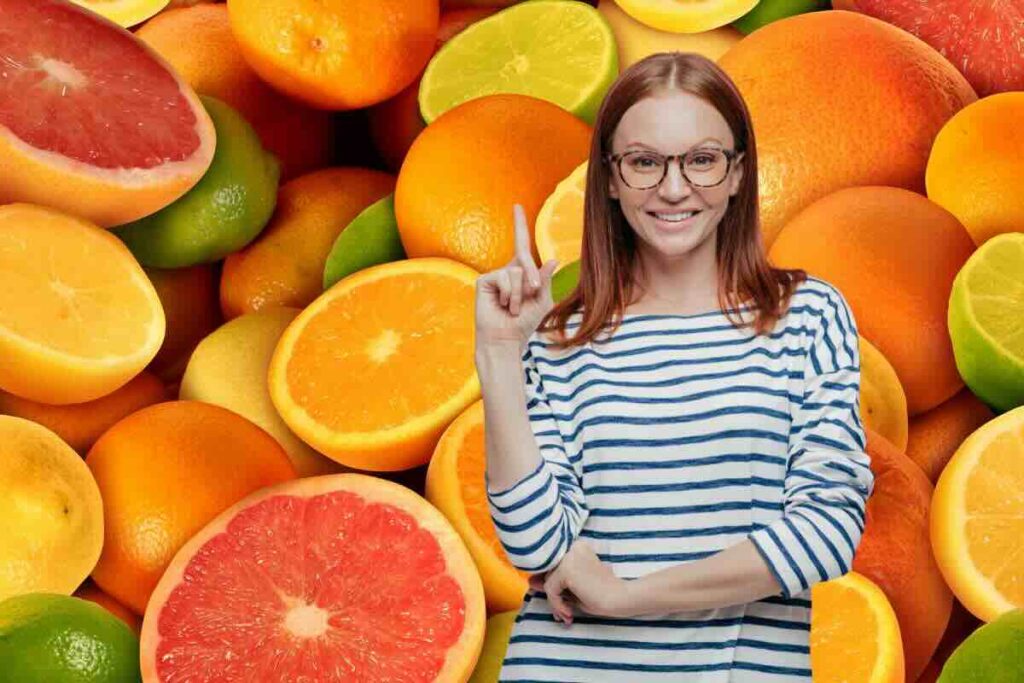 Agrumi sullo sfondo e in primo piano donna con dito rivolto verso l'alto, sorridente