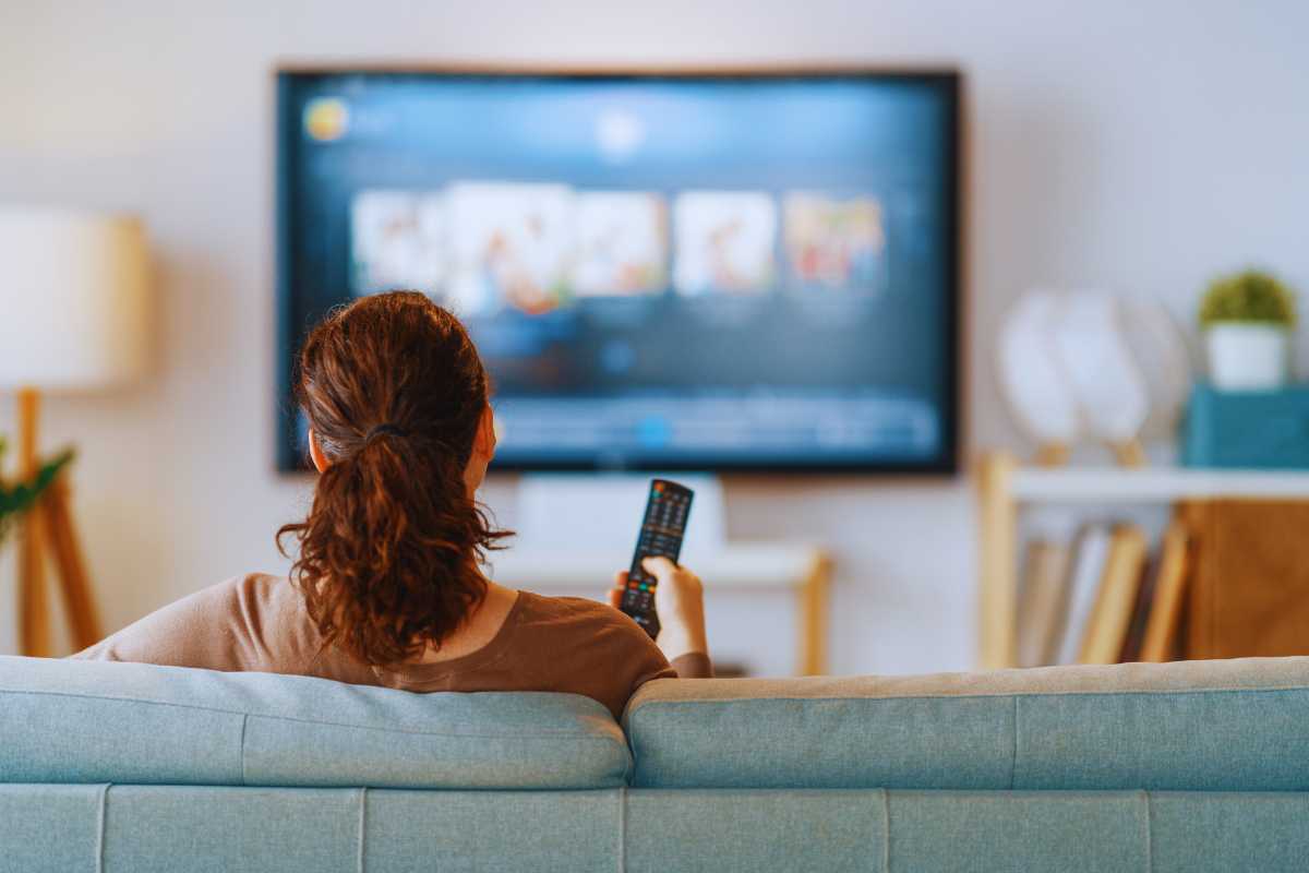 Donna seduta sul divano che guarda la TV con il telecomando in mano