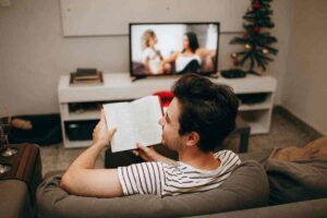 Uomo seduto sul divano che guarda la tv con un libro in mano