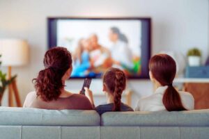 Tre persone di schiena sedute sul divano che guardano la TV